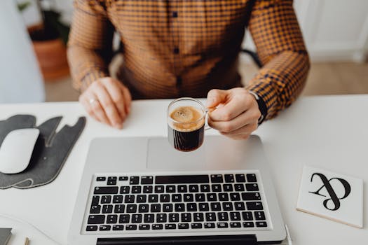 A person holding espresso near laptop and mouse, ideal for work from home themes.